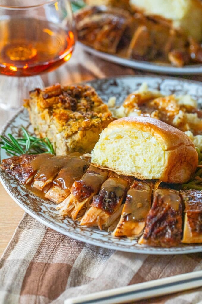 sliced turkey breast with gravy on plate with dinner roll