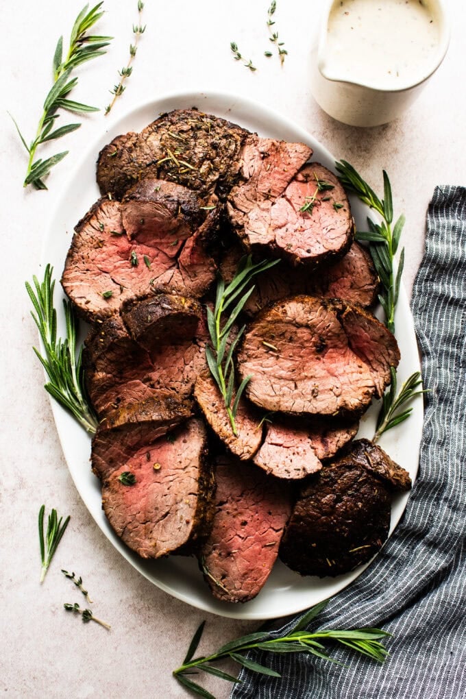 sliced beef tenderloin on white platter with herbs