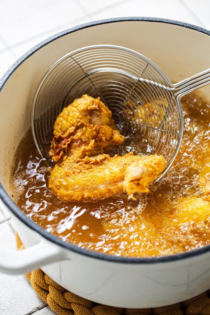 fried chicken wing in pot of hot oil cooking with strainer