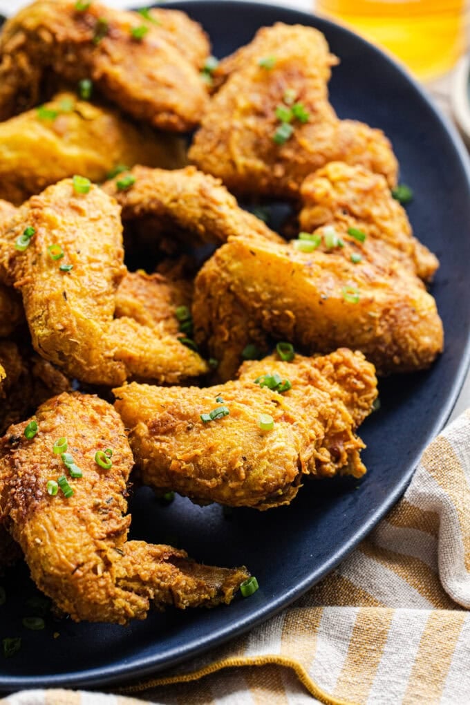 closeup of fried curry chicken wings with chopped scallions on platter