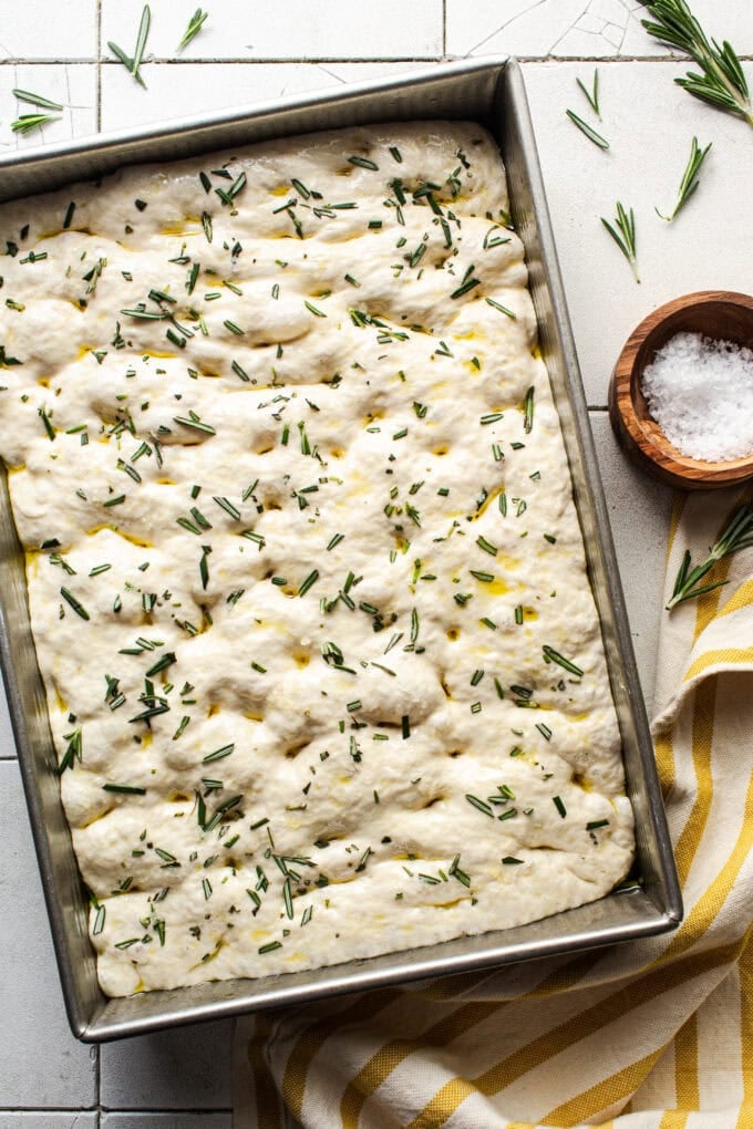 raw focaccia dough with chopped rosemary in pan