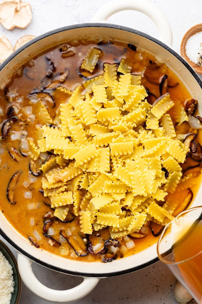 raw pasta in pot with broth and mushrooms
