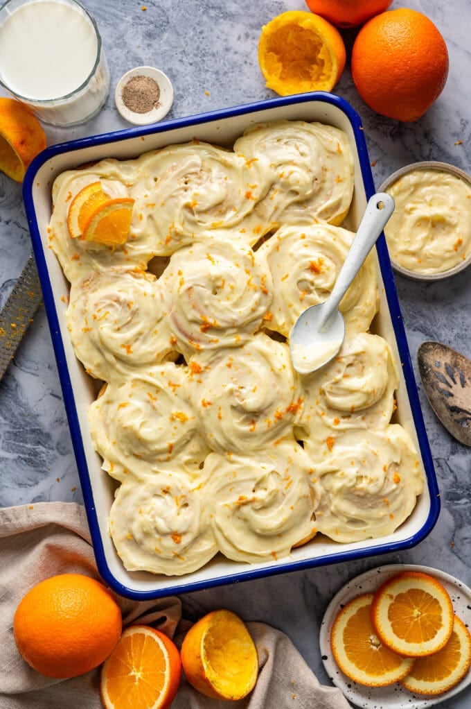 frosted orange sweet rolls in baking pan with serving spoon