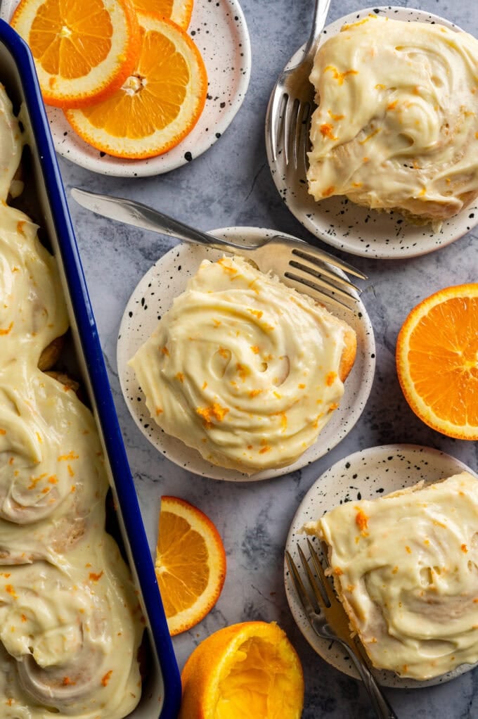 frosted orange sweet rolls on small plates with forks