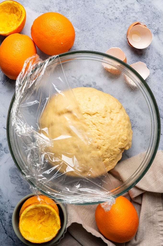 orange yeasted dough in glass bowl with plastic wrap