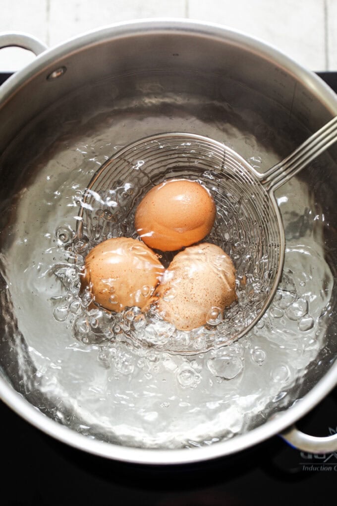 three eggs on strainer going into boiling water