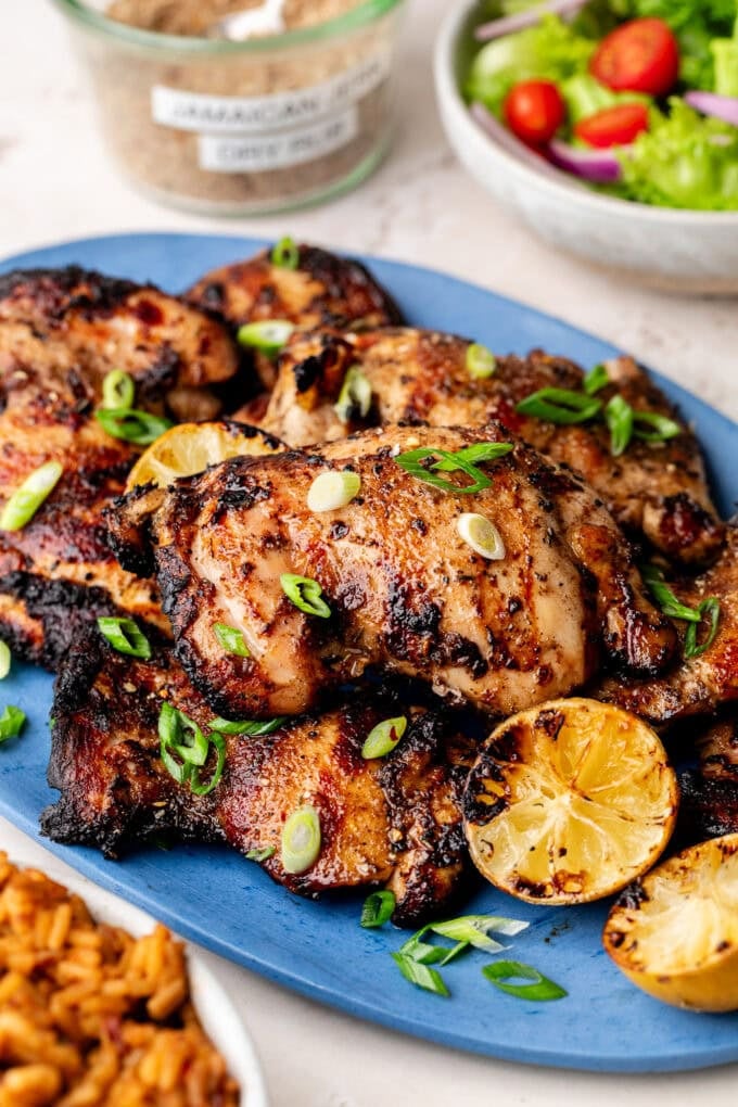 grilled jerk chicken thighs on blue platter with lemon