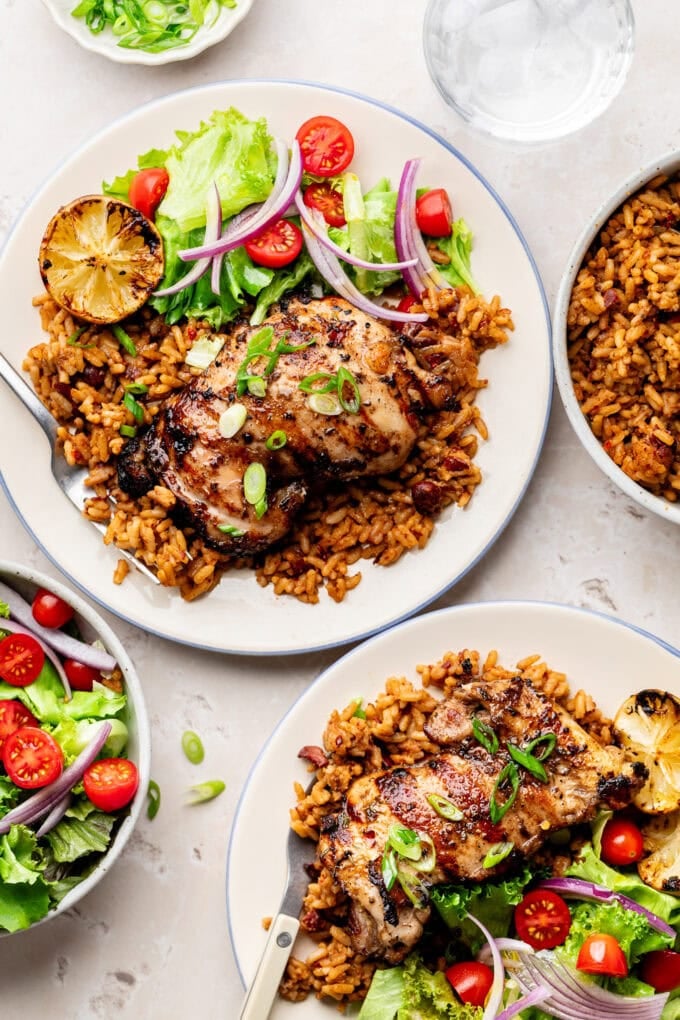 grilled jerk chicken thighs with rice and salad on plates
