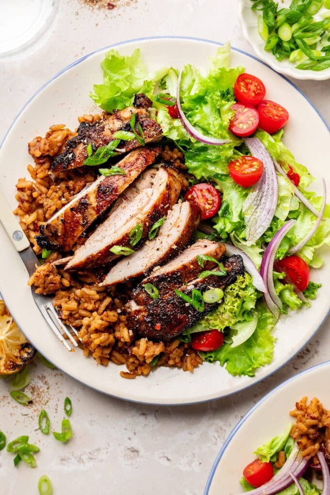 sliced grilled jerk chicken on rice with salad