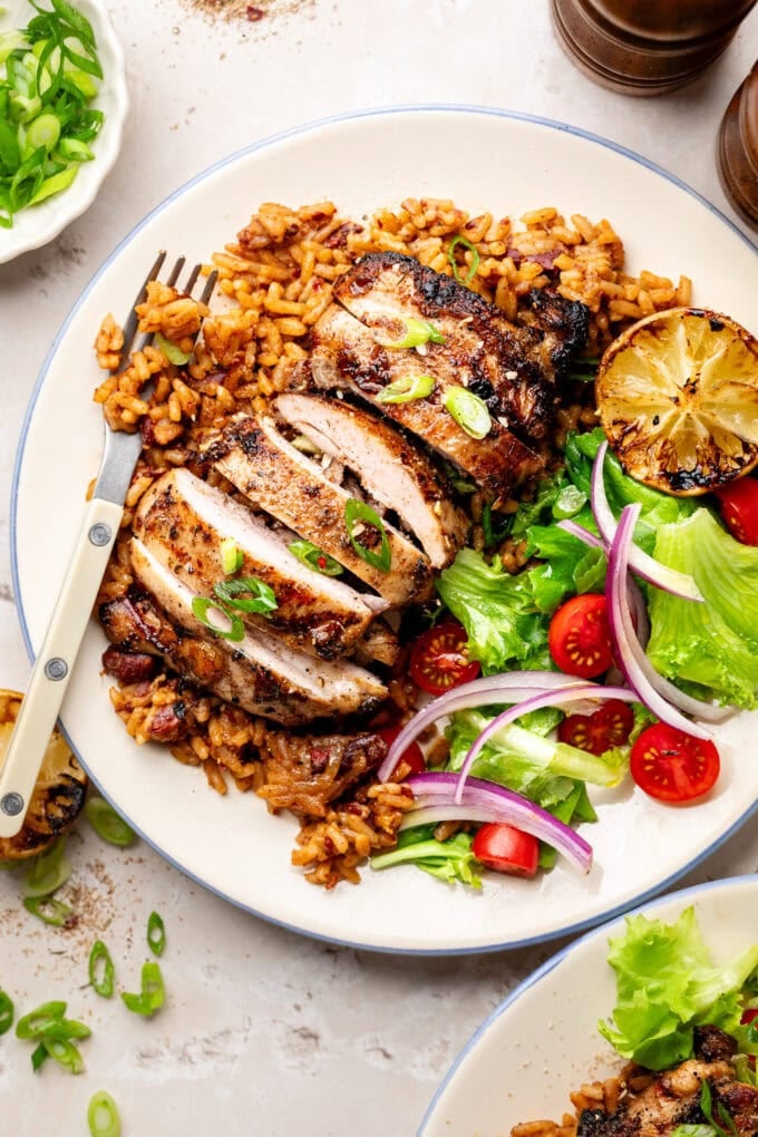 grilled jerk chicken thighs with rice and salad on white plate