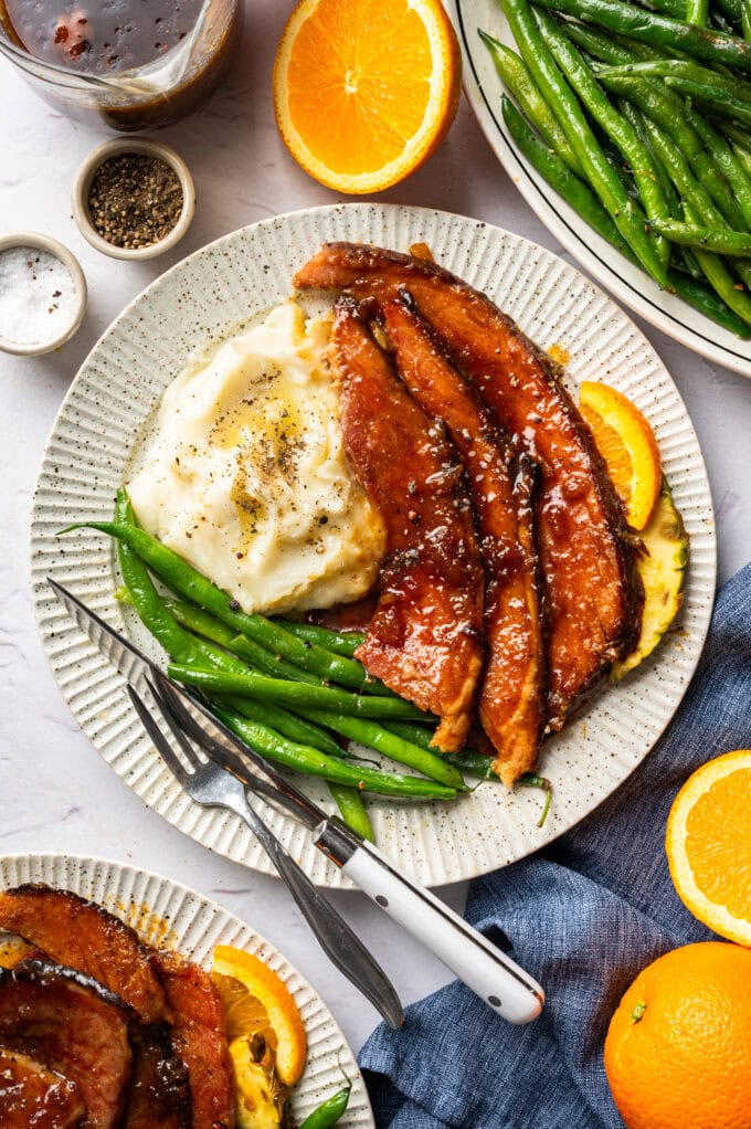 sliced glazed ham on plate with mashed potatoes and green beans
