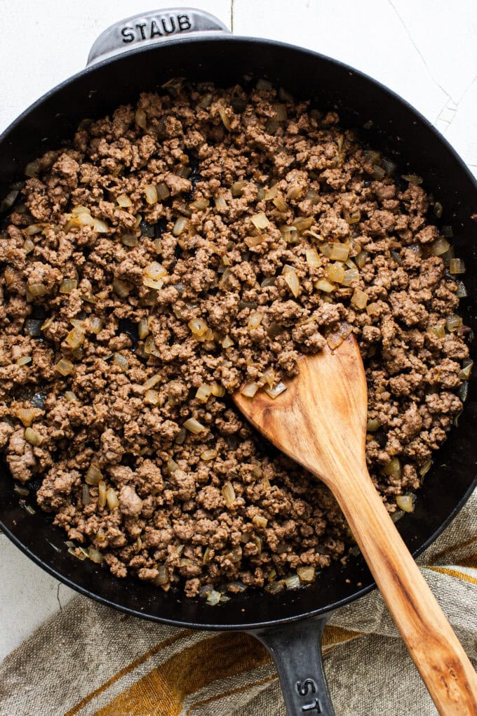 ground beef and onion in skillet with wooden spatula