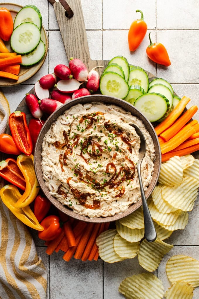 caramelized onion dip in bowl with chips and veggies around it