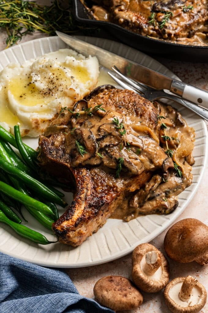 smothered pork chops with mushrooms on plate with green beans and mashed potatoes