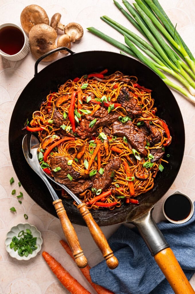 steak lo mein in black wok with serving utensils