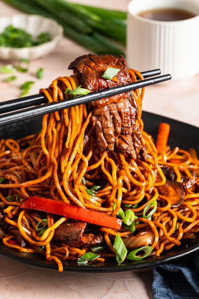 black chopsticks holding steak lo mein over bowl