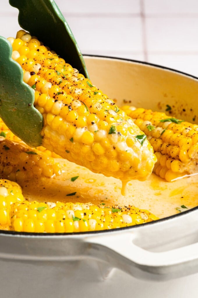 tongs holding creamy corn on the cob