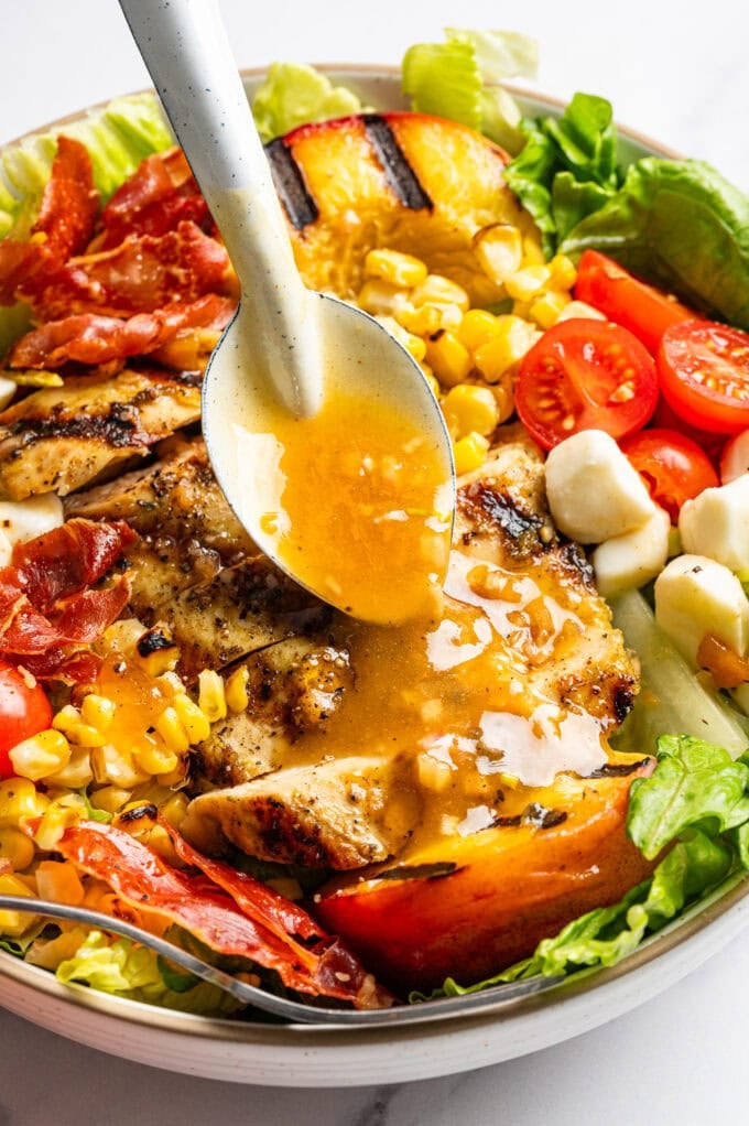spoon pouring peach shallot vinaigrette over salad