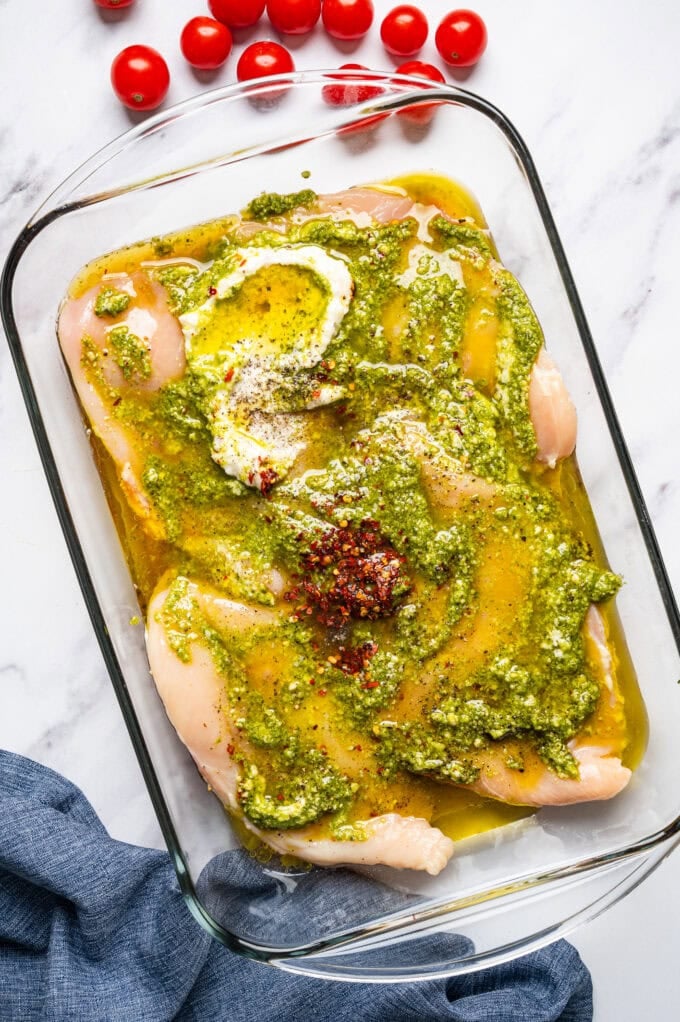 raw chicken breasts with pesto and spices in glass bowl