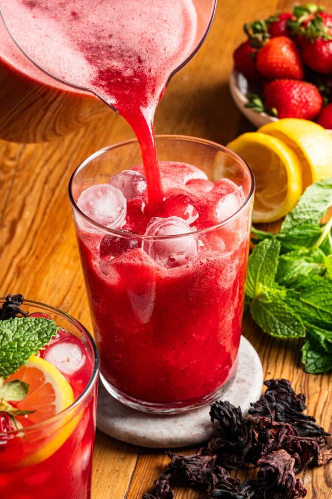 strawberry hibiscus lemonade being poured into glass with ice