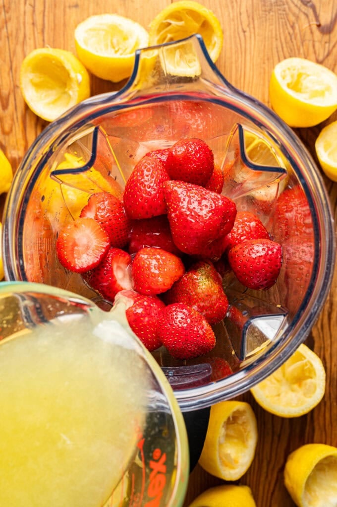 lemon juice being poured into blender with strawberries