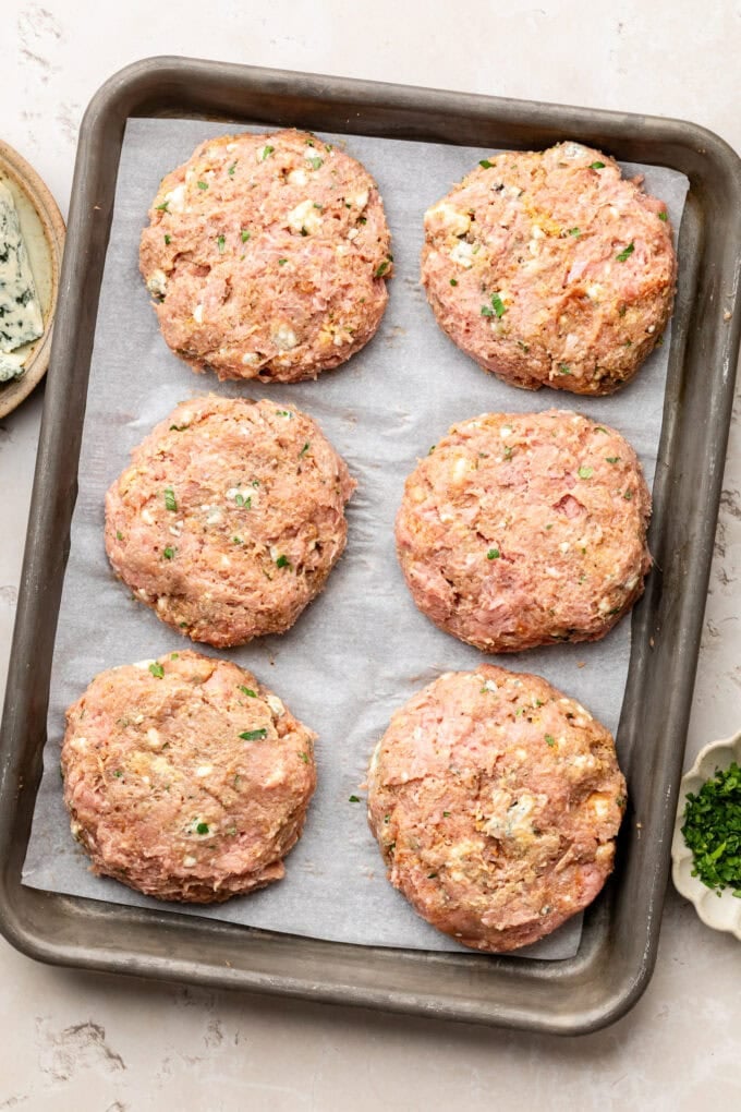 raw shaped turkey burger patties on baking sheet