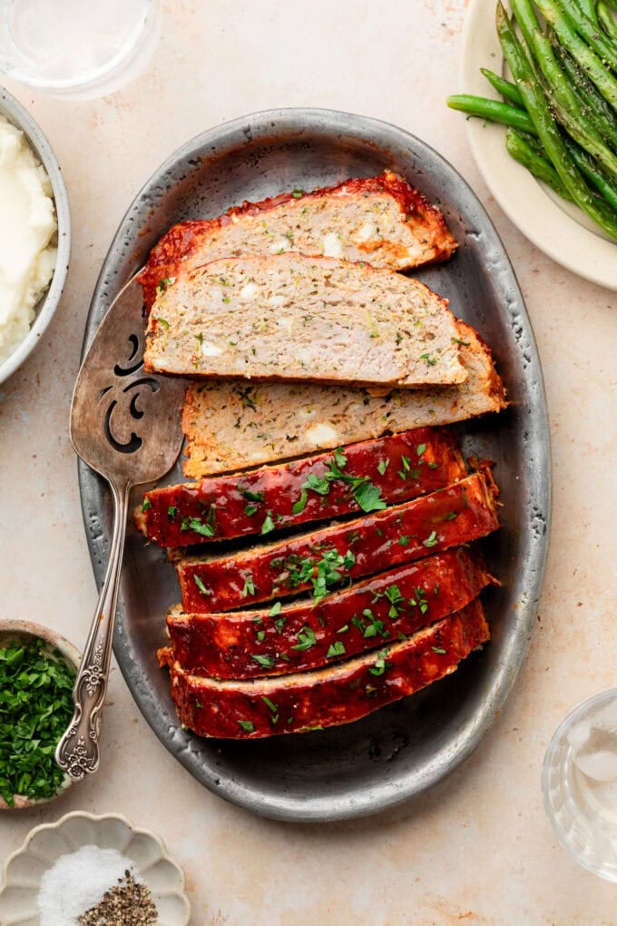 zucchini feta meatloaf sliced on silver platter with serving utensil
