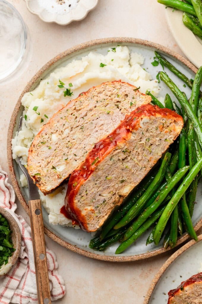 sliced zucchini feta meatloaf with mashed potatoes and green beans on plate