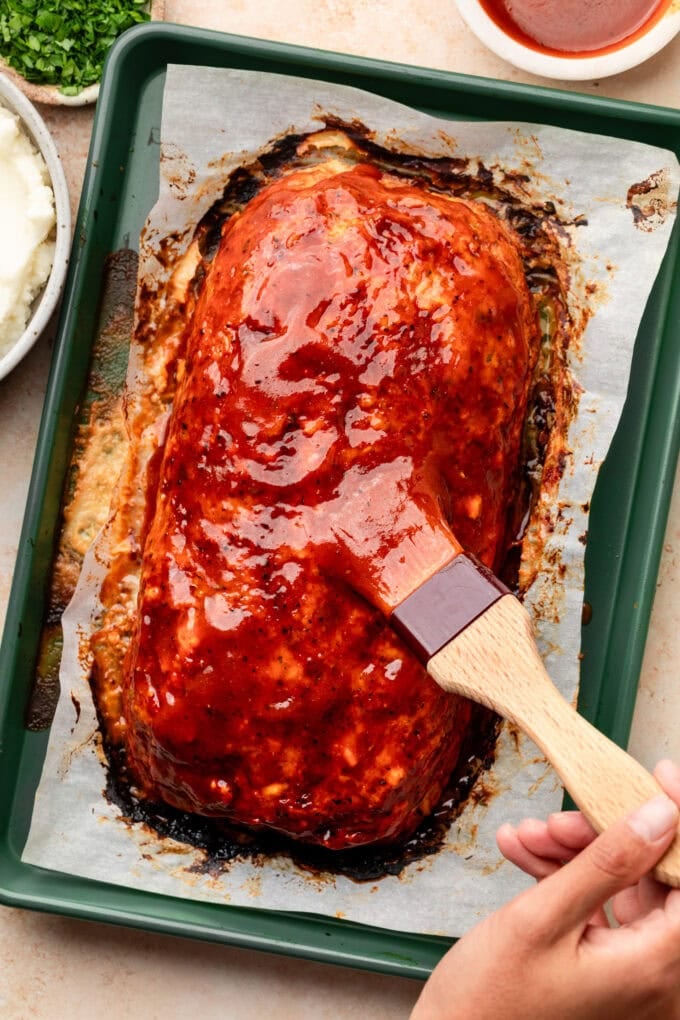 hand brushing bbq sauce over meatloaf