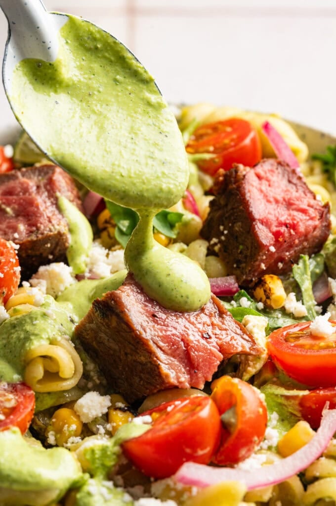 spoon pouring jalapeno crema over steak pasta salad