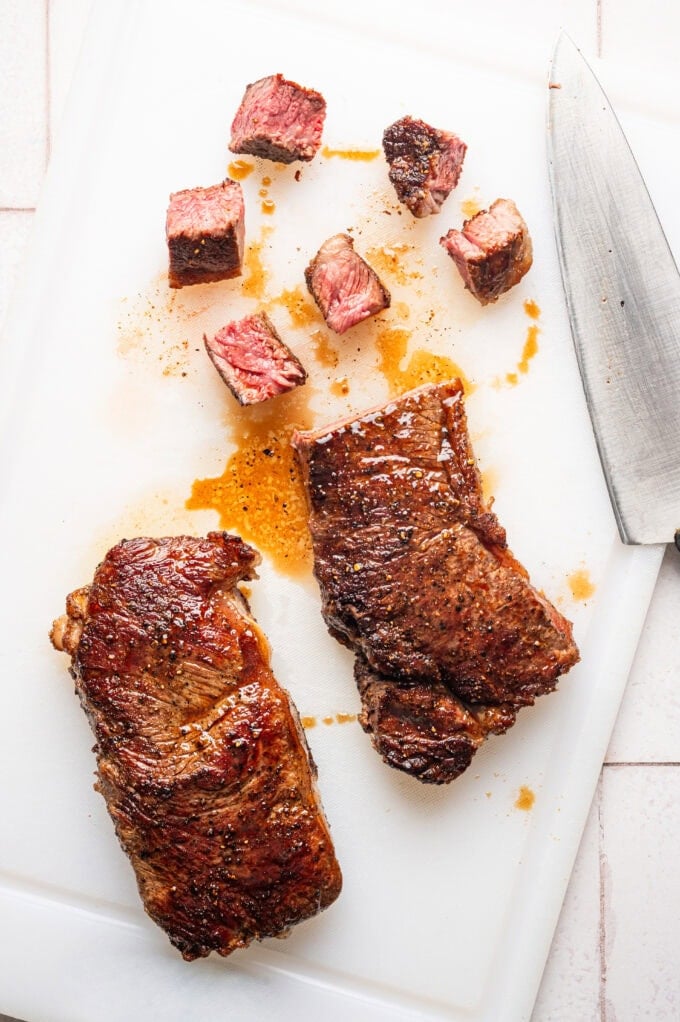 seared steak on cutting board cubed with knife