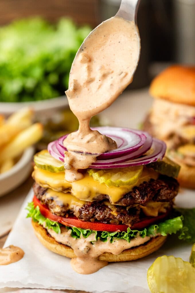 spoon pouring burger sauce over smash burger