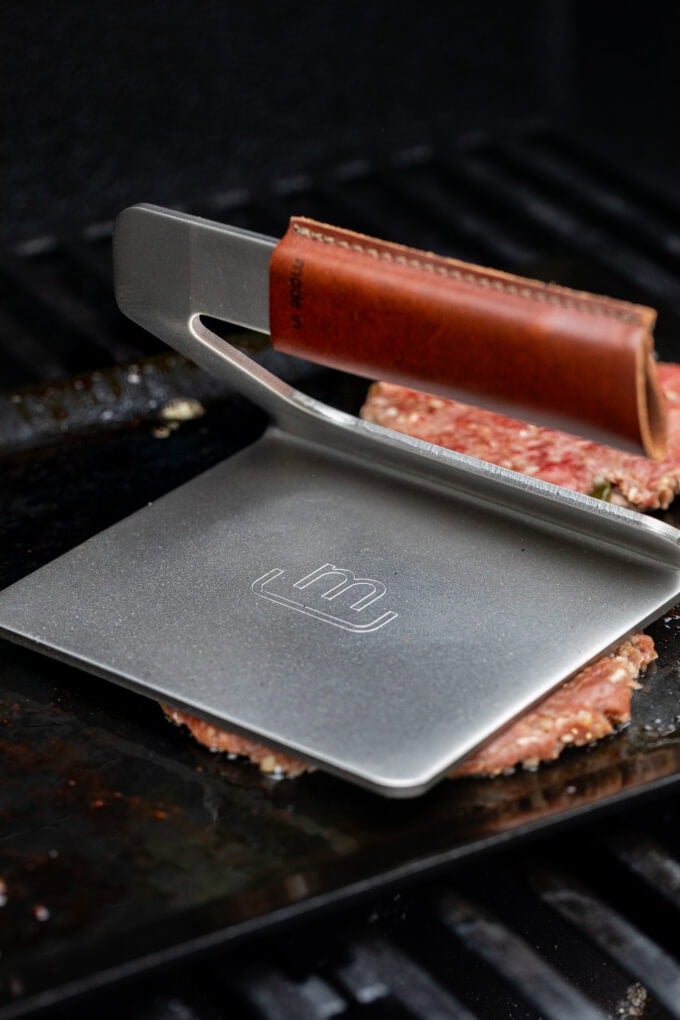 meat press on raw burger patty on grill
