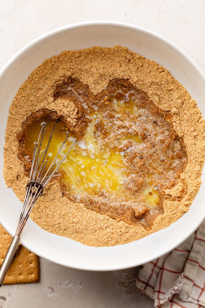 crushed graham crackers and melted butter in bowl with whisk