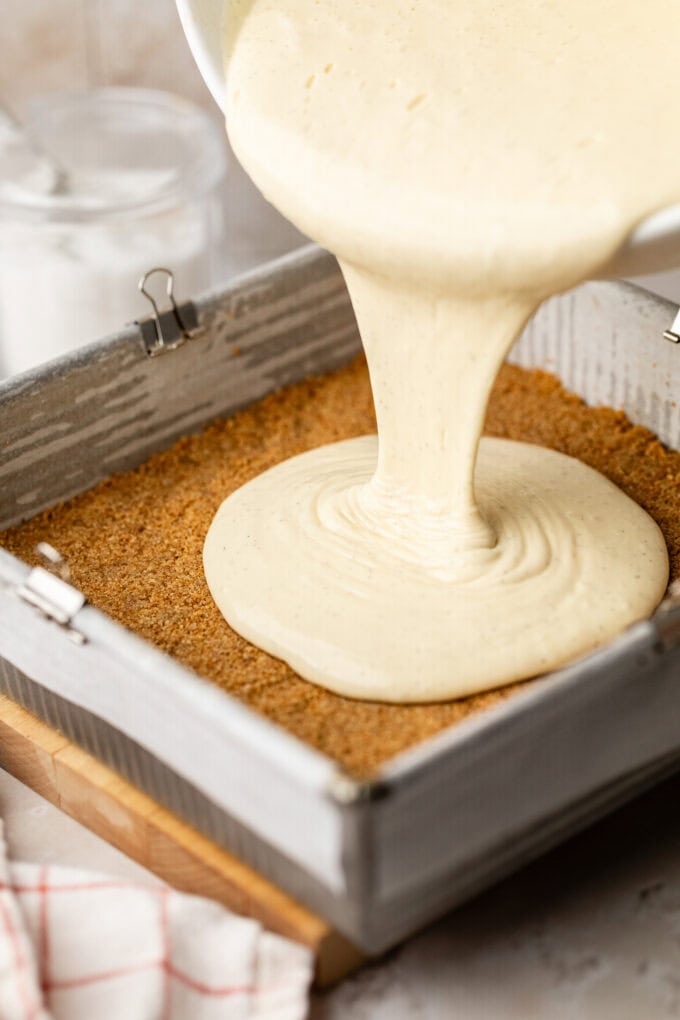 cheesecake batter being poured onto graham cracker crust