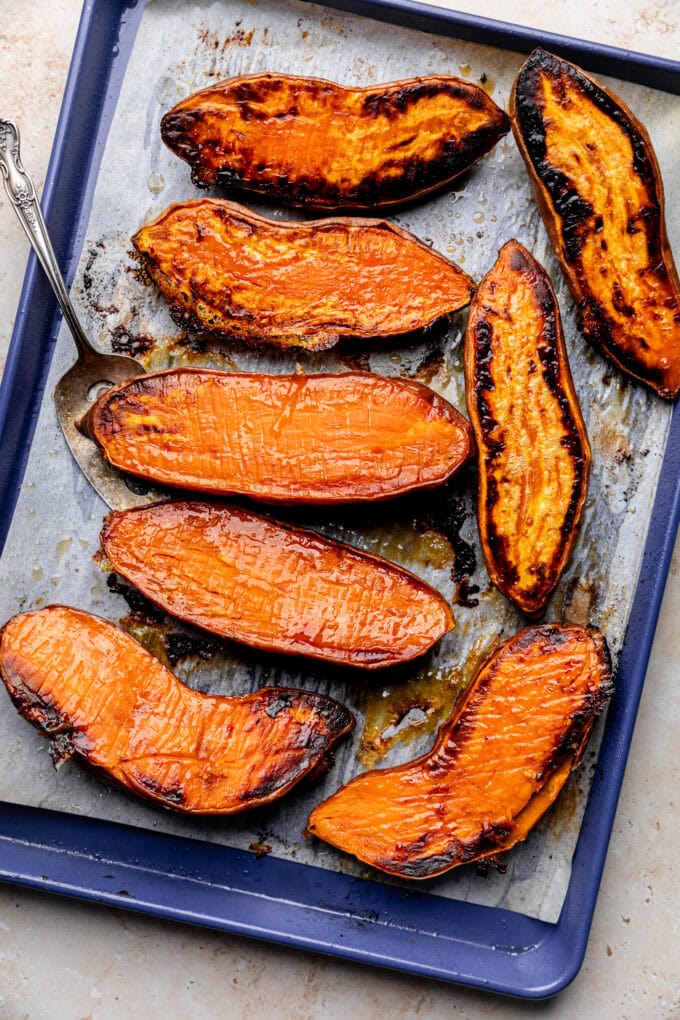 roasted sweet potato halves on baking sheet with serving utensil
