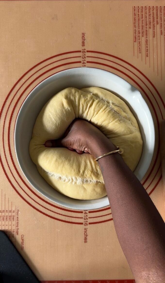 black hand punching down yeast dough in bowl