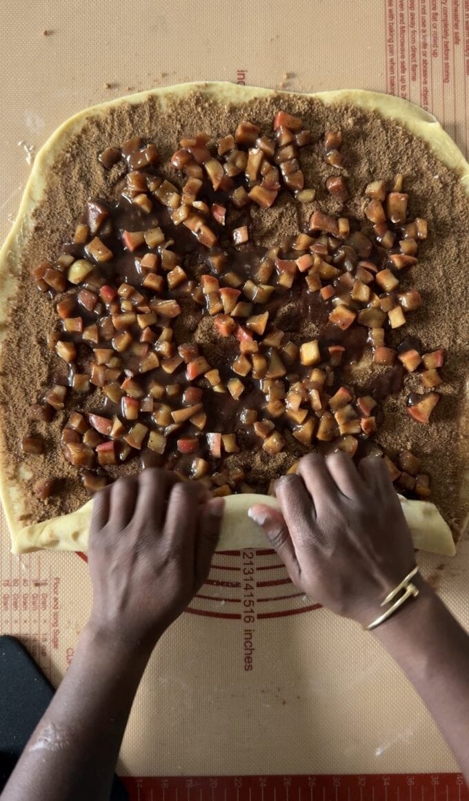 black hands rolling up apple cinnamon roll dough
