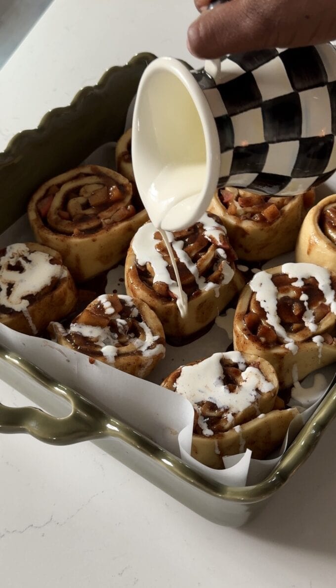 cream being poured over unbaked cinnamon rolls