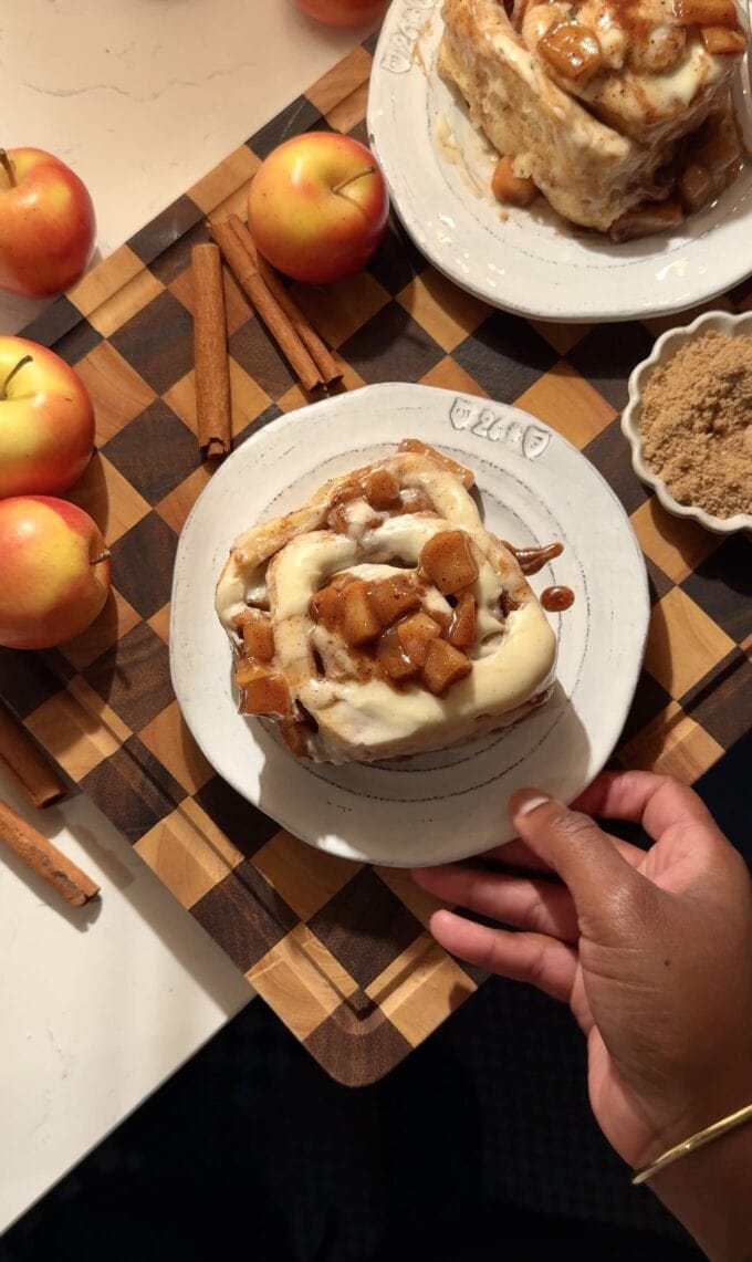 black hand holding plate with apple cinnamon roll