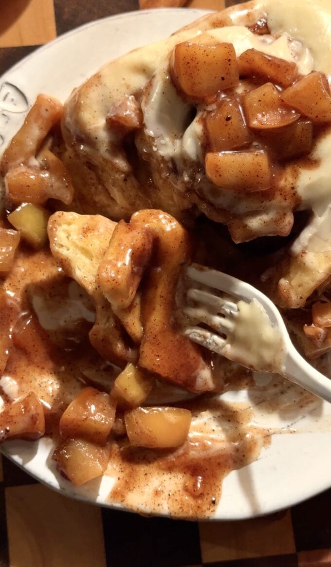white fork cutting into apple cinnamon roll on plate