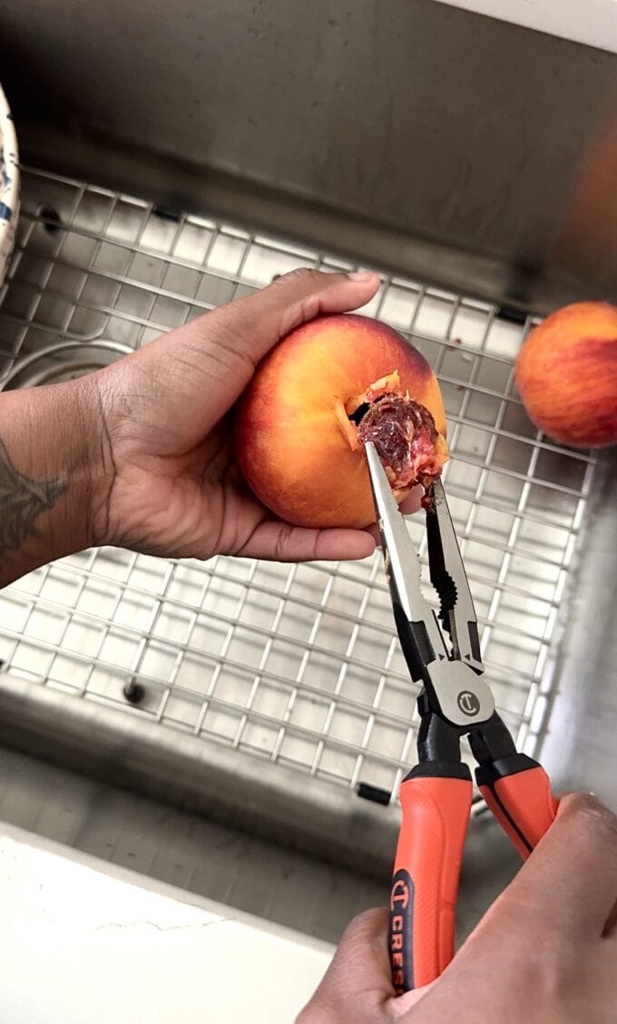 black hand pitting peach over sink