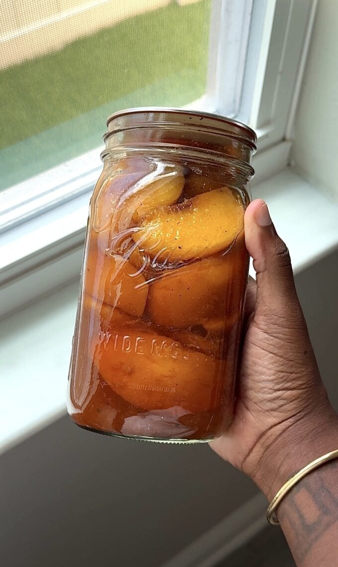 black hand holding jar of sweet tea peaches
