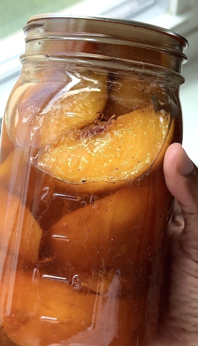 black hand holding jar of sweet tea peaches